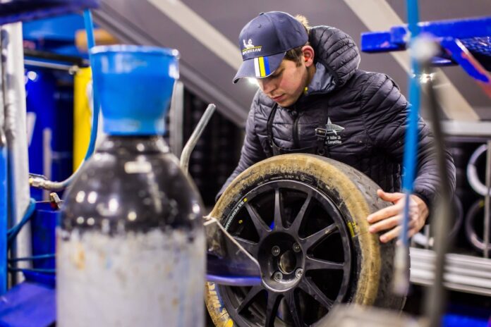 Ein Mitarbeiter in einer Kfz-Werkstatt hält einen Reifen in der Hand um ihn zu wechseln.