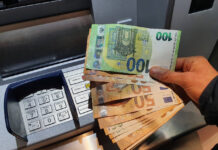 Eine Hand hält mehrere 50-Euro-Scheine und einen Hunderter über einen Geldautomaten. Der Kunde hat das Bargeld bei der Bank abgeholt und steht am Geldautomaten. Das Geld wird von seinem Konto abgebucht.