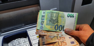 Eine Hand hält mehrere Euro-Scheine über einem Geldautomaten. 700 Euro Zuschuss vom Staat können Arbeitnehmer jetzt beantragen.