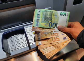 Eine Hand hält mehrere Euro-Scheine über einem Geldautomaten. 700 Euro Zuschuss vom Staat können Arbeitnehmer jetzt beantragen.