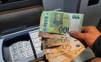 Eine Hand hält mehrere Euro-Scheine über einem Geldautomaten.