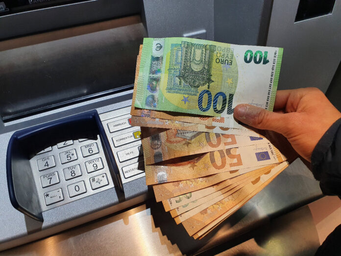 Eine Hand hält mehrere Euro-Scheine über einem Geldautomaten.