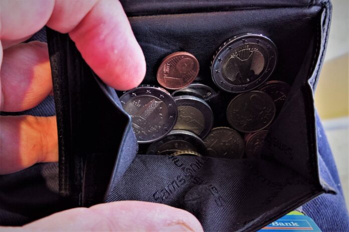 Jemand hält ein kleines Portemonnaie, das mit Kleingeld gefüllt ist. Im Geldbeutel enthalten sind mehrere Münzen, Geldscheine fehlen. Wahrscheinlich möchte die Person mit dem Geld bezahlen.
