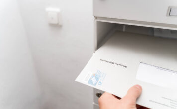 Eine Hand nimmt einige Briefe aus dem Briefkasten.