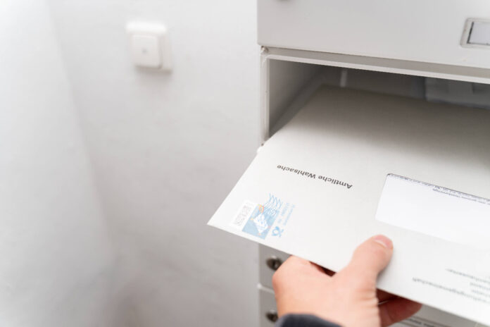 Eine Hand nimmt einige Briefe aus dem Briefkasten.