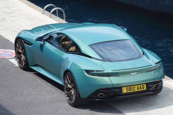 Ein türkiser Aston Martin steht neben Wasser am Hafen.