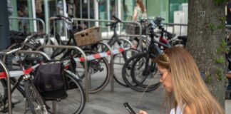 Mehrere Fahrräder stehen nebeneinander auf einem abgesperrten Gebiet, eine Frau schaut auf ihr Handy