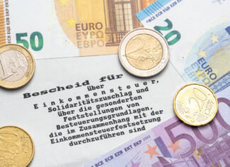 Auf einem Steuerbescheid vom Finanzamt liegen Euro-Müzen und Euro-Scheine.