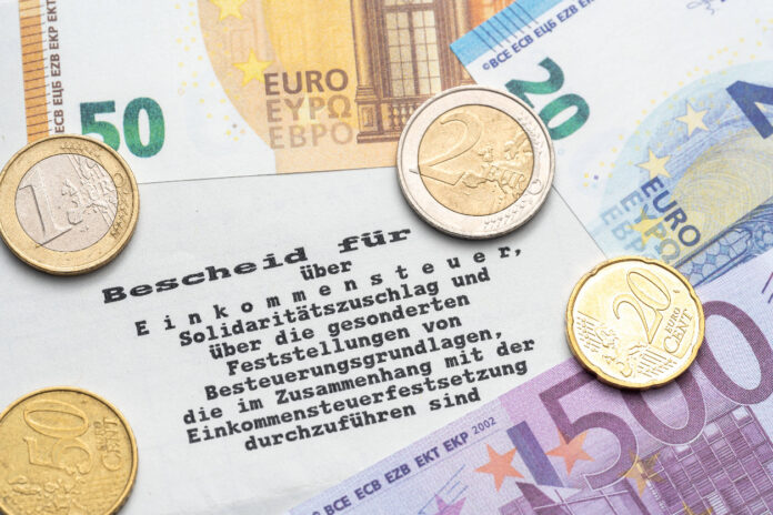 Auf einem Steuerbescheid vom Finanzamt liegen Euro-Müzen und Euro-Scheine.