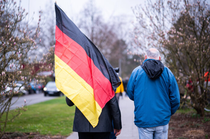 Zwei Menschen gehen mit einer Deutschland-Flagge einen Weg entlang.