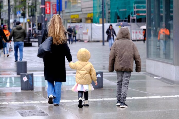 Eine Familie geht in der Innenstadt spazieren. Die Mutter hält die Hand des Kindes.