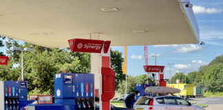 Eine überdachte Synergy Tankstelle bei schönem Wetter in der Natur in Deutschland, mit mehreren Zapfsäulen und Fahrzeugen davor, die betankt werden wollen. An der Zapfsäule stehen mehrere Autos, die Benzin oder Diesel tanken.