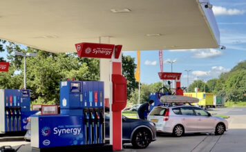 Eine überdachte Synergy Tankstelle bei schönem Wetter in der Natur in Deutschland, mit mehreren Zapfsäulen und Fahrzeugen davor, die betankt werden wollen. An der Zapfsäule stehen mehrere Autos, die Benzin oder Diesel tanken.