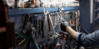 Ein Mechaniker nimmt in einer Werkstatt Werkzeug von einer Wand. An der Wand hängen Zangen, Schraubenzieher und andere Werkzeuge für Heimwerker.