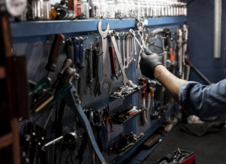 Ein Mechaniker nimmt in einer Werkstatt Werkzeug von einer Wand. An der Wand hängen Zangen, Schraubenzieher und andere Werkzeuge für Heimwerker.