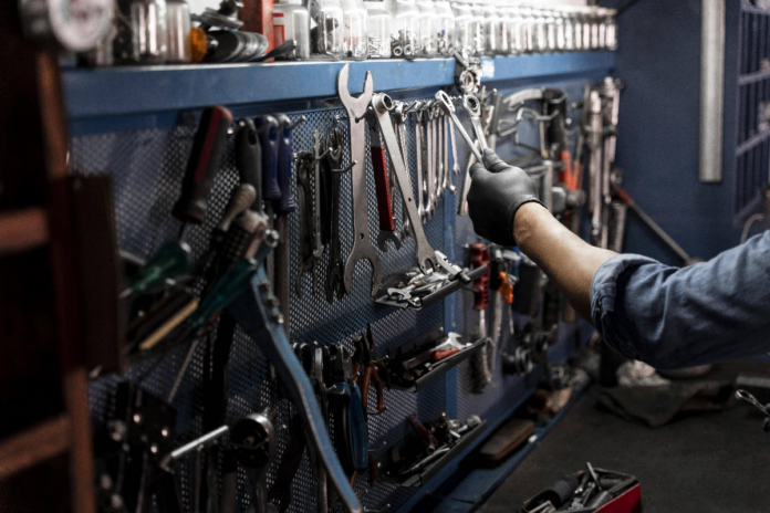 Ein Mechaniker nimmt in einer Werkstatt Werkzeug von einer Wand. An der Wand hängen Zangen, Schraubenzieher und andere Werkzeuge für Heimwerker.