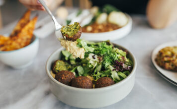 Eine Person isst eine Falafel-Bowl mit Gemüse und Salat. Im Hintergrund stehen gesunde vegane und vegetarische Snacks auf dem Tisch.