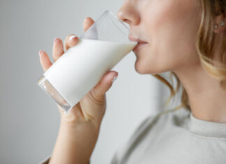 Das Close-Up einer Frau, welche ein Glas Milch trinkt. Die Milch in dem Glas ist halbvoll und die Fingernägel der Frau haben den selben milchweißen Farbton wie die Milch.