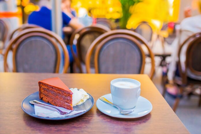 Ein Stückkuchen oder ein Stück Torte auf einem Teller neben einer Tasse mit Milch oder einem Cappuccino.