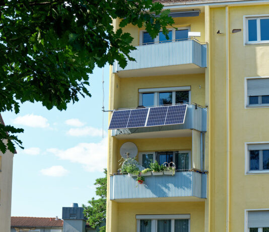 Eine kleine PV-Anlage wurde an einem Balkon befestigt, dieser befindet sich an einem gelben Hochhaus