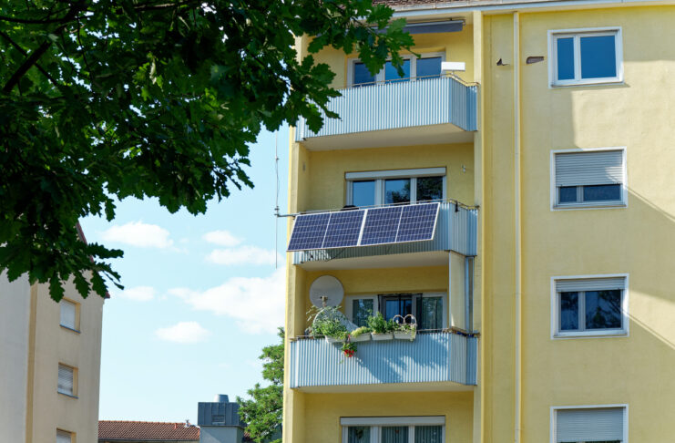 Eine kleine PV-Anlage wurde an einem Balkon befestigt, dieser befindet sich an einem gelben Hochhaus