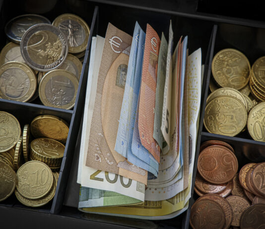 Eine Kasse ist vollgefüllt mit Euro-Münzen und Euro-Scheinen.