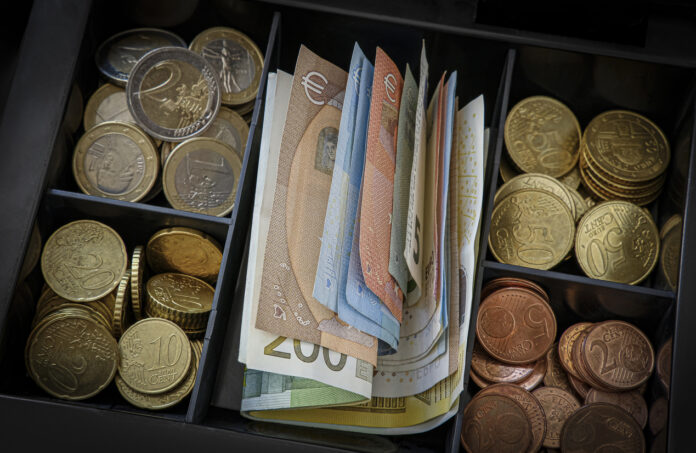 Eine Kasse ist vollgefüllt mit Euro-Münzen und Euro-Scheinen.