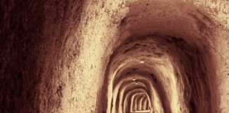 Zu sehen ist ein höhlenähnlicher, langer Tunnel aus Stein und Sand. Dieser ist beleuchtet.