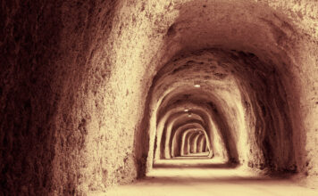 Zu sehen ist ein höhlenähnlicher, langer Tunnel aus Stein und Sand. Dieser ist beleuchtet.