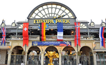 Der Eingang zum Europa-Park in Rust, an dem Flaggen mehrerer Länder hängen. Davor steht eine große goldene Statue unter einem der Bögen.