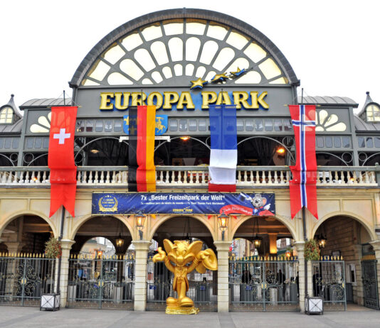 Der Eingang zum Europa-Park in Rust, an dem Flaggen mehrerer Länder hängen. Davor steht eine große goldene Statue unter einem der Bögen.