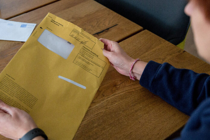 Eine unkenntliche Person hält einen gelb-braunen A4-Umschlag in den Händen. Darin befindet sich ein offizieller Brief, der Millionen Haushalten zugeschickt wurde.