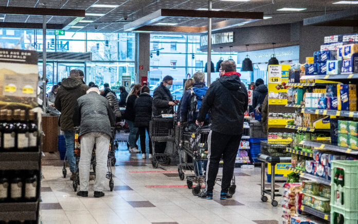 Einige Kunden stehen mit ihren Einkaufswagen in langen Schlangen an den Kassen in einem Supermarkt und warten, bis sie ihre Waren auf das Band legen können.