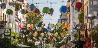 Mehrere Bürger und Passanten gehen durch eine bunt geschmückte Straße in Karlsruhe an einem schönen Tag. Es findet gerade ein großes Straßenfest oder ein Kulturfest statt, weshalb so viele Menschen unterwegs sind.