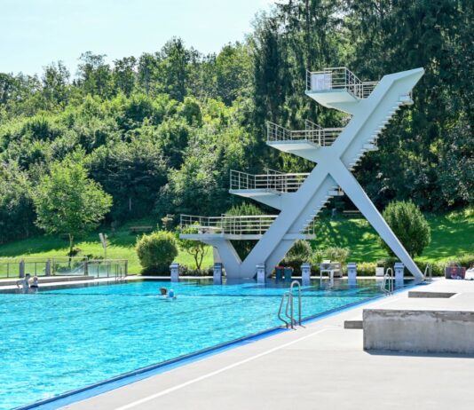 Ein großes Schwimmbad und ein Schwimmbecken mit einer Wasserrutsche und einem Springturm im Sommer