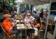 Gäste im Außenbereich eines Restaurants. Die Gäste sitzen geschützt auf der Terrasse. Sie genießen ihre Getränke und Speisen, die der Kellner zum Tisch bringt.