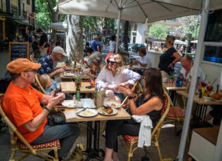 Gäste im Außenbereich eines Restaurants. Die Gäste sitzen geschützt auf der Terrasse. Sie genießen ihre Getränke und Speisen, die der Kellner zum Tisch bringt.