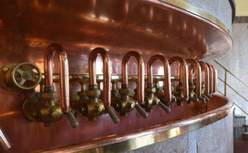 In einer Brauerei steht ein riesiger Kessel mit einer Menge Zapfhähne in einer Reihe.