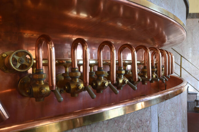 In einer Brauerei steht ein riesiger Kessel mit einer Menge Zapfhähne in einer Reihe.