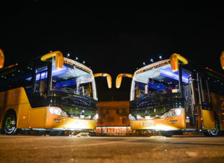 Zwei Busse stehen nebeneinander in der Nacht, beide Reisebusse haben das Licht angeschaltet.