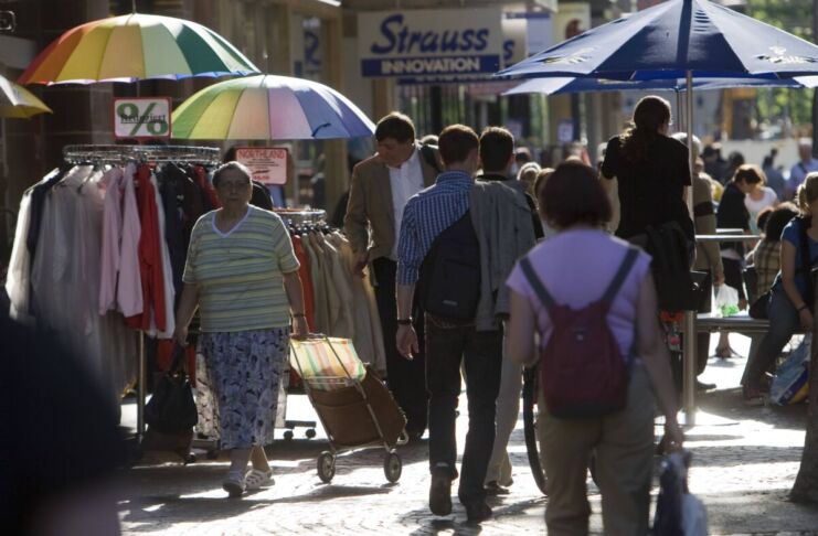 Viele Passanten schlendern durch die Sonne, einige halten einen bunten Sonnenschirm in der Hand. Sie kaufen in einigen Geschäften der Innenstadt ein und betrachten die Auslagen der Händler.