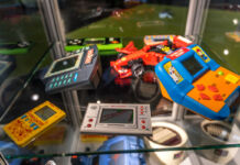 In einem gläsernen Schaukasten sind mehrere Handheld Konsolen, Retro Konsolen, Nintendo und Gameboys ausgestellt. Bunt und sichtbar alt sind sie für eine Ausstellung über das Gaming gedacht.