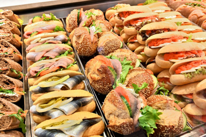 Eine große, reiche Auslage mit belegten Brötchen und Snacks an einem Imbiss oder Bistro. Lachs, Forelle mit Zwiebel, Salatblätter, Krabbenbrötchen und mehr finden sich im Sortiment der Fischbrötchen