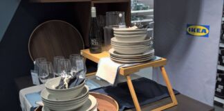 Gestapelte weiße, schicke Teller, Gabel, Messer und Löffel von IKEA liegen auf mehreren Holztischen und sind für Kunden des Möbel-Einrichtungshauses zum Kauf verfügbar.