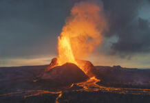Ein gewaltiger Vulkanausbruch, festgehalten auf Kamera, bei dem Feuer aus dem Berg strömt und heiße, glühend rote Lava auf die aufgerissene Erde fließt.