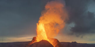 Ein gewaltiger Vulkanausbruch, festgehalten auf Kamera, bei dem Feuer aus dem Berg strömt und heiße, glühend rote Lava auf die aufgerissene Erde fließt.