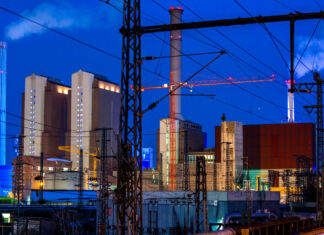 Ein Blick auf ein Industriegebiet in der Abenddämmerung. Man erkennt mehrere Fabrikgebäude aus denen Dampf kommt. Es handelt sich dabei um ein Heizkraftwerk, welches Kohle und Erdgas verbrennt.