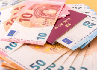 Viele Geldscheine europäischer Währung liegen auf einem Tisch. Es liegen 50-Euro-Schein, 10-Euro-Scheine und 20-Euro-Scheine Bargeld bereit. In dem kleinen Häufchen Geld liegt außerdem ein Reisepass.