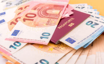 Viele Geldscheine europäischer Währung liegen auf einem Tisch. Es liegen 50-Euro-Schein, 10-Euro-Scheine und 20-Euro-Scheine Bargeld bereit. In dem kleinen Häufchen Geld liegt außerdem ein Reisepass.