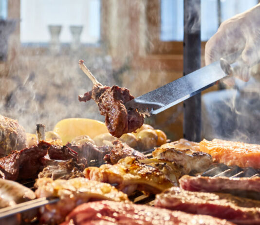 Das Fleisch wird auf den Grill gelegt, Rippchen, Würste, Hühnchen. Es handelt sich um ein Grillgericht. Verschiedene Portionen Fleisch werden gegart und den Gästen serviert.